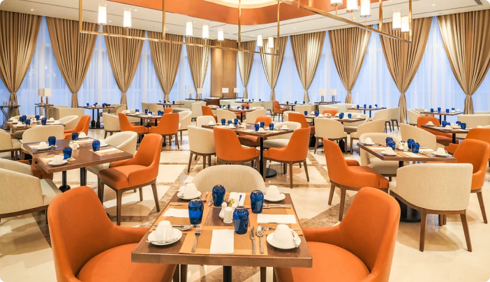주황색 의자와 고급스러운 테이블이 세팅되어 있는 21 All Day Dining 레스토랑 내부 모습